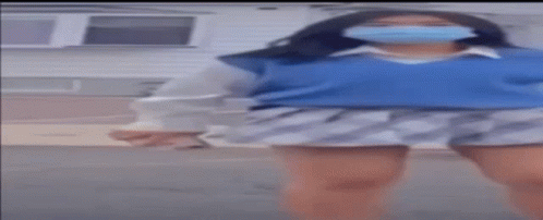 A Woman Wearing A Mask And A Blue Sweater Is Dancing In Front Of A House . GIF