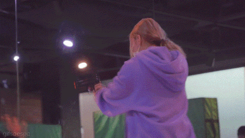 a woman wearing a mask and a purple hoodie is standing in a room