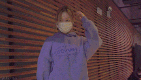 a woman wearing a mask and a purple hoodie is standing in front of a wooden wall .
