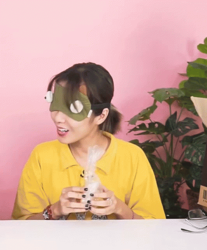 A Woman Wearing A Mask And A Yellow Shirt Is Holding A White Object GIF
