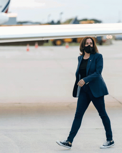 A Woman Wearing A Mask And Converse Shoes Walks On An Airport Tarmac GIF