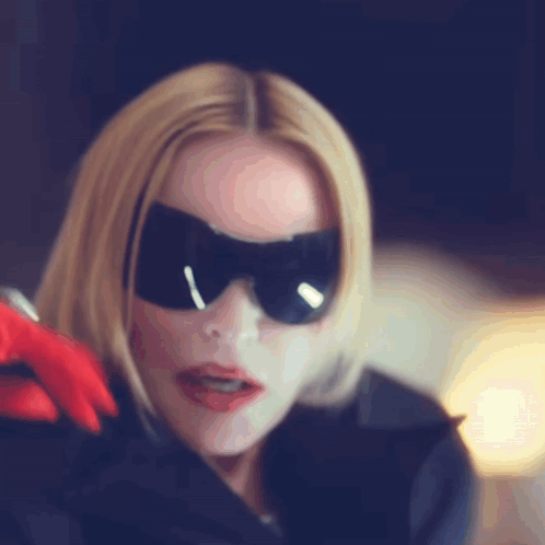 A Woman Wearing A Mask And Sunglasses Is Holding A Red Glove GIF