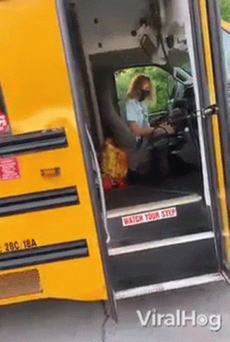 A Woman Wearing A Mask Is Driving A School Bus With The Door Open . GIF