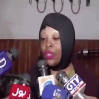 A Woman Wearing A Mask Is Talking Into Microphones . GIF