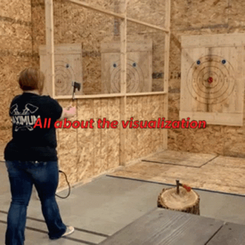 A Woman Wearing A Maximum Shirt Is Throwing An Axe At A Target GIF