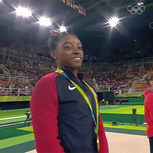 A Woman Wearing A Medal Around Her Neck Stands In Front Of A Crowd At The Olympics GIF