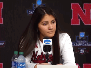a woman wearing a nebraska shirt is sitting at a desk with a microphone