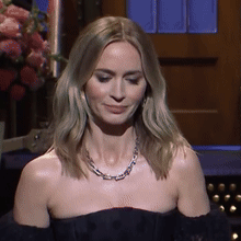 A Woman Wearing A Necklace And A Black Dress Is Smiling GIF