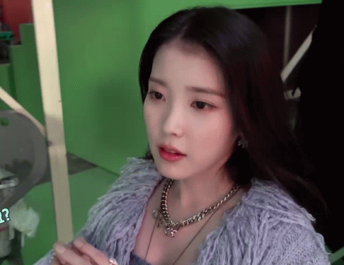 a woman wearing a necklace and a purple sweater looks at the camera