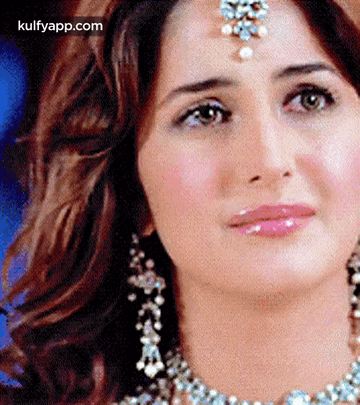A Woman Wearing A Necklace And Earrings Is Looking At The Camera . GIF