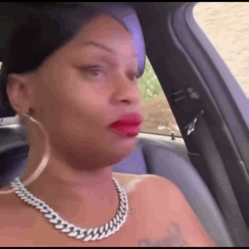 a woman wearing a necklace and earrings is sitting in a car making a funny face .