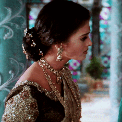 A Woman Wearing A Necklace And Earrings With A Bun GIF