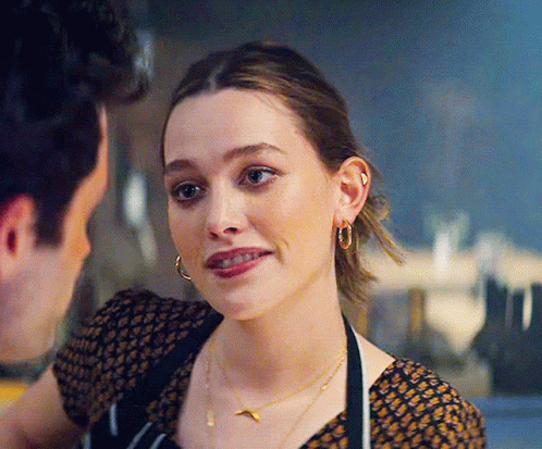 A Woman Wearing A Necklace And Hoop Earrings Is Looking At A Man . GIF