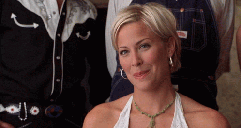 A Woman Wearing A Necklace And Hoop Earrings Is Smiling In Front Of A Man In A Cowboy Shirt GIF