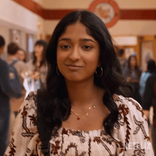 A Woman Wearing A Necklace And Hoop Earrings Is Standing In A Crowded Hallway . GIF