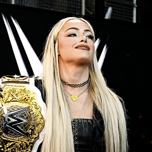 A Woman Wearing A Necklace That Says I Love You Is Holding A Wrestling Belt GIF