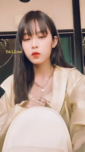 A Woman Wearing A Necklace With A Padlock On It Is Holding A White Backpack And Has The Word Yellow Written On Her Face GIF