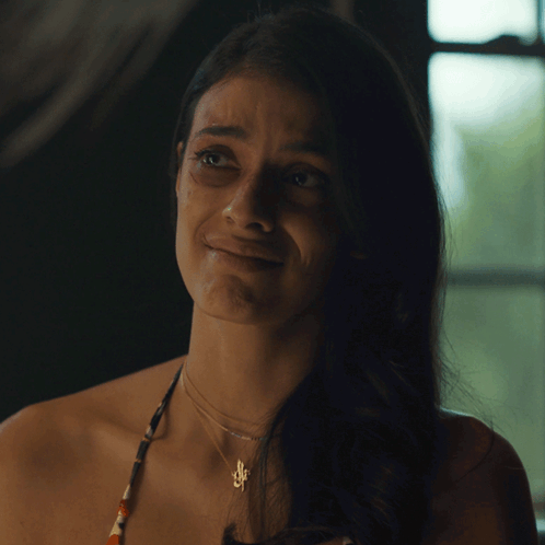 A Woman Wearing A Necklace With A Pendant That Says S On It GIF