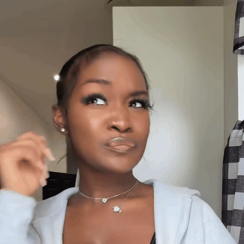 A Woman Wearing A Necklace With A Planet On It Looks At The Camera GIF