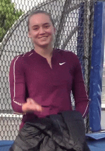 A Woman Wearing A Nike Shirt Is Smiling And Holding A Black Jacket GIF