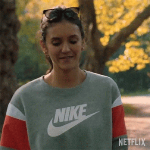 A Woman Wearing A Nike Sweatshirt And Sunglasses Is Smiling In A Park . GIF