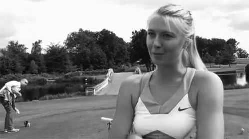 A Woman Wearing A Nike Tank Top Is Standing In A Park GIF