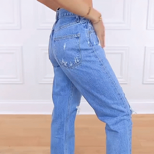 A Woman Wearing A Pair Of Ripped Jeans Stands With Her Hands In Her Pockets GIF