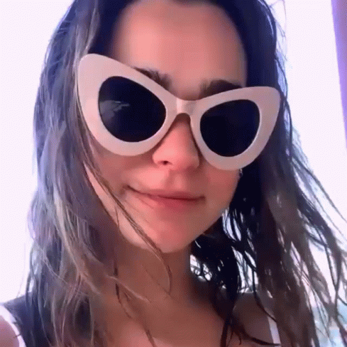 a woman wearing a pair of white cat eye sunglasses looks at the camera