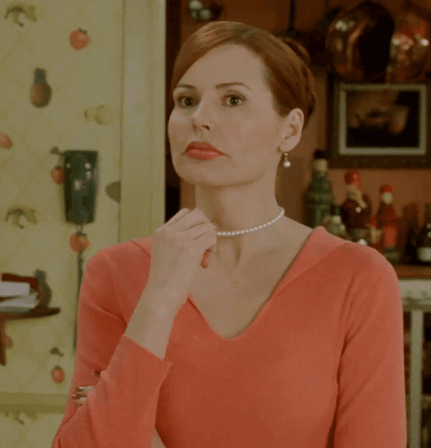 A Woman Wearing A Pearl Necklace And A Red Shirt GIF