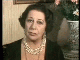 A Woman Wearing A Pearl Necklace And Earrings Is Looking At The Camera . GIF