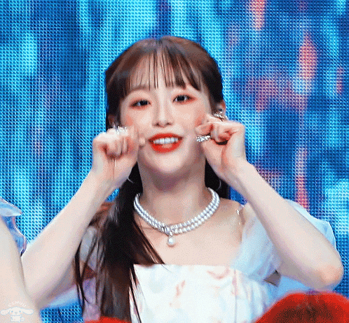 A Woman Wearing A Pearl Necklace And Earrings Looks At The Camera GIF