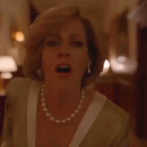 A Woman Wearing A Pearl Necklace And Gloves Is Standing On A Red Carpet In A Room . GIF
