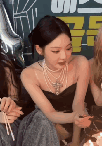 A Woman Wearing A Pearl Necklace Is Sitting Next To A Cake With Candles GIF