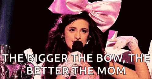 A Woman Wearing A Pink Bow And Gloves Is Talking Into A Microphone . GIF
