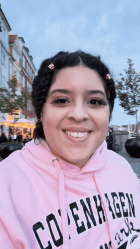 A Woman Wearing A Pink Copenhagen Hoodie Smiles GIF
