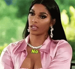 A Woman Wearing A Pink Shirt And A Necklace With The Word No On It Is Sitting On A Chair . GIF