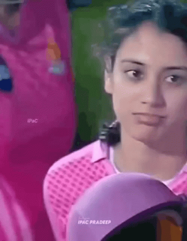 A Woman Wearing A Pink Shirt And A Purple Hat Is Looking At The Camera . GIF