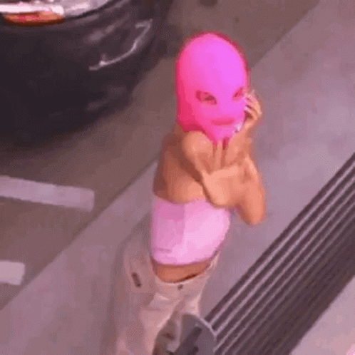A Woman Wearing A Pink Ski Mask Is Standing In Front Of A Car . GIF