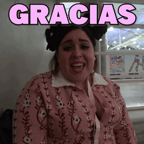 A Woman Wearing A Pink Sweater With The Word Gracias Above Her GIF