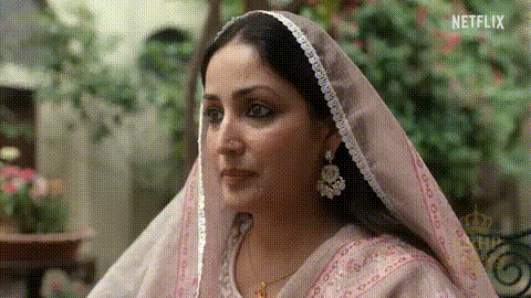 A Woman Wearing A Pink Veil And Earrings Is Looking At Something . GIF