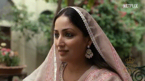 A Woman Wearing A Pink Veil And Earrings Is Looking At The Camera . GIF