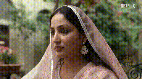 A Woman Wearing A Pink Veil And Earrings Is Sitting Down . GIF