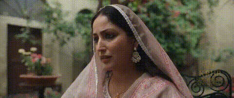 A Woman Wearing A Pink Veil And Earrings Is Sitting On A Chair . GIF
