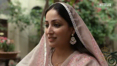 A Woman Wearing A Pink Veil And Earrings Is Smiling And Looking At The Camera . GIF