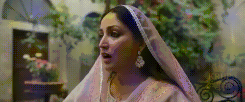 A Woman Wearing A Pink Veil And Earrings Is Standing In A Room . GIF