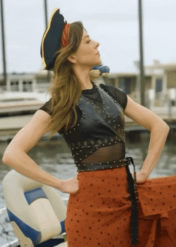 A Woman Wearing A Pirate Hat Is Standing In Front Of A Body Of Water GIF