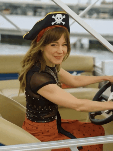 A Woman Wearing A Pirate Hat With A Skull And Crossbones On It Is Driving A Boat GIF