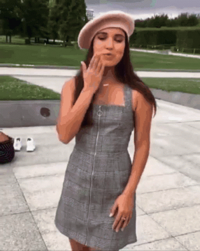 A Woman Wearing A Plaid Dress And A Beret Blows A Kiss GIF