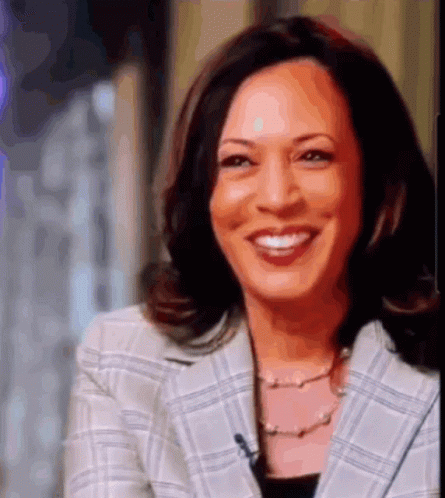 A Woman Wearing A Plaid Jacket And A Pearl Necklace Is Smiling GIF