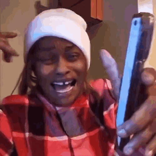 a woman wearing a plaid shirt and a beanie is holding a cell phone .